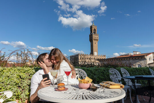 Happy couple with smartphone resting in garden near tower