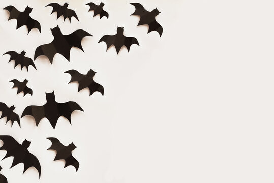 Halloween holiday decorations of many paper bats flying over an empty white background with free space for text. Top view.