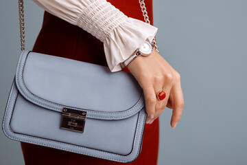 Close up of fashionable elegant woman`s outfit: trendy small blue faux leather bag, stylish wrist...