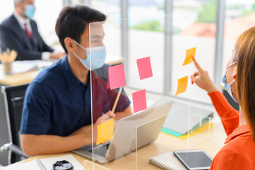 Asian businesspeople with glass board and post it note for coronavirus covid-19 protection working...