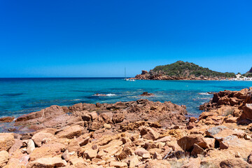 landscape, red rock above a blue bay in the beach of Su Sirboni