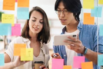 Image of multinational colleagues using mobile phone and marker pen