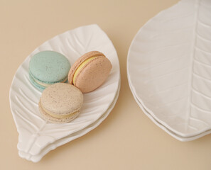Macarons in white plate on beige background.