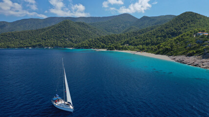 Aerial drone photo of sailing boat cruising near famous turquoise paradise beach of Milia covered with pine trees, Skopelos island, Sporades, Greece