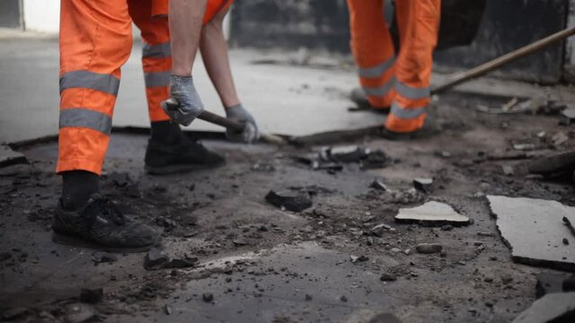 The workers are fixing the road. Men are breaking the asphalt. Construction work on the street. People in overalls with shovels.