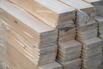A bunch of natural wooden planks prepared for construction and protected from the rain with a plastic cover