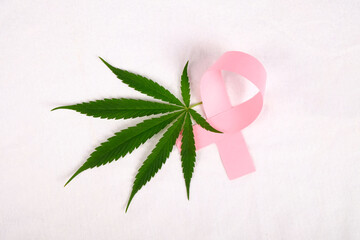 pink ribbon and green leaf of marijuana medical plant on white background. cannabis cancer...