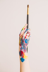 Woman's hand smeared with paints holding paintbrush. Close-up photography for ad of art school or art blog © Georgii