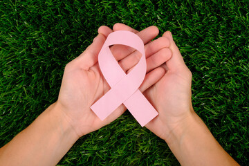 pink ribbon on the palms on a green background. Cancer awareness concept