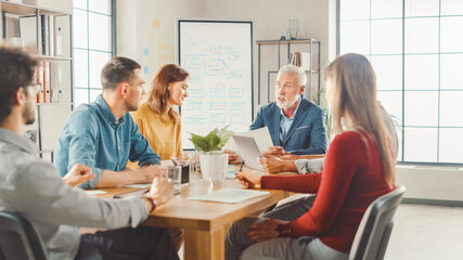 In the Meeting Room Team of Businesspeople, Entrepreneurs and Specialists sitting at the Conference Table Have Discussions, Solve Problems, Use Tablet, Laptop, Share Documents with Statistics, Charts