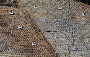 A close up view of wire netting and bolts containing a rock face.