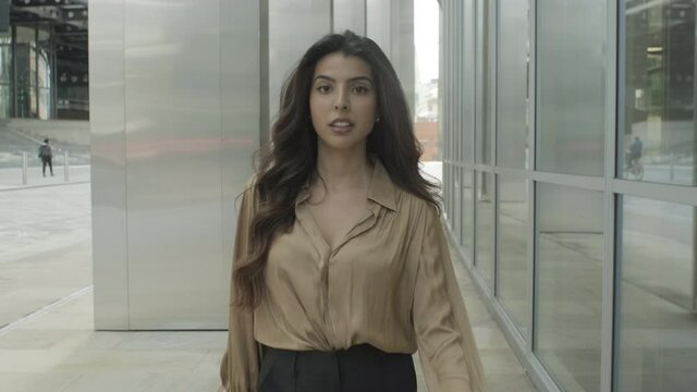 Portrait of confident young adult business woman walking in city and looking to camera, female executive moving up successful corporate career ladder