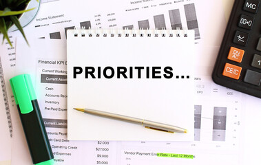 Notepad with text PRIORITIES on a white background, near calculator and office supplies. Business...