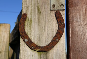 A close up view of a rusty horseshoe nailed to a wooden gate post.