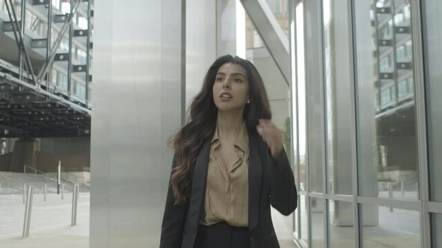 Ambitious successful Hispanic Young adult business woman walking outside office in city wearing suit