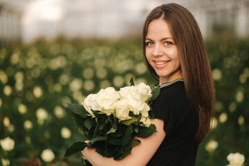 Portrait of beautiful young woman in greenhouse with bouquet of white roses
