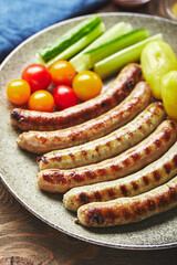 asty grilled sausages with potato and vegetables on plate in a close up view on wooden background. Top view, flat lay.