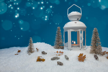 White Christmas lantern on snow with pine cones, small cones, leaves, golden christmas trees and a fir branch in front of dark blue background