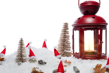 Red Christmas lantern on snow with pine cones, small cones, leaves, golden christmas trees, small golden baubles with santa hats in front of a white background, copy space