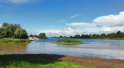 Obraz premium sunny landscape with blue sky over green river bank with moored boats