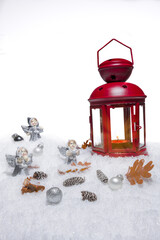 Red Christmas lantern on snow with small cones, leaves, silver choralling angles in front of white background, copy space