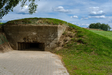 An old abandoned defensive bunker (zot) in the park, during the Second World War, against the background of a field and sky with clouds.