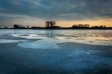 Water puddles on the frozen lake and clouds after sunset