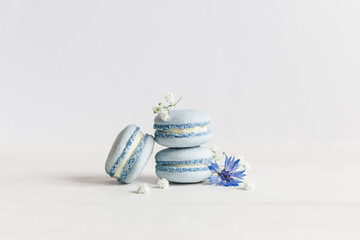 Fototapeta premium Tasty blue french macarons with flowers on a white wooden background.