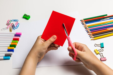 Child hands cutting colored paper with scissors at the table