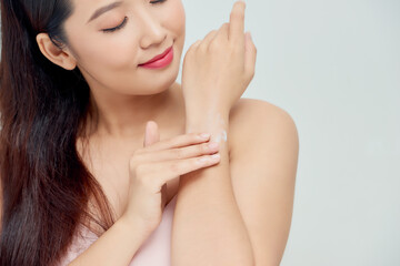 Plakat Smiling young woman applies cream on her hands. On a white background.