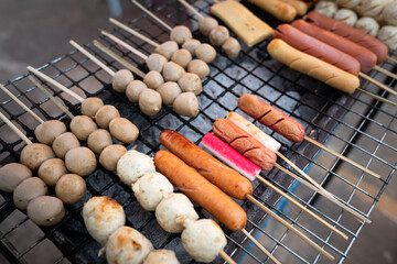 Stick of sausage and meat ball are grilling on coal, Traditional Thai style BBQ food which is sale in local market. Street photo, selective focus at the sausage's part.