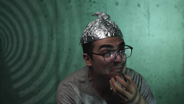 Insane men wearing a tin foil hat to protect himself from the 5g waves hitting his brain being afraid and scarred looking around him. Conspiracy theory making a person loose touch with reality.