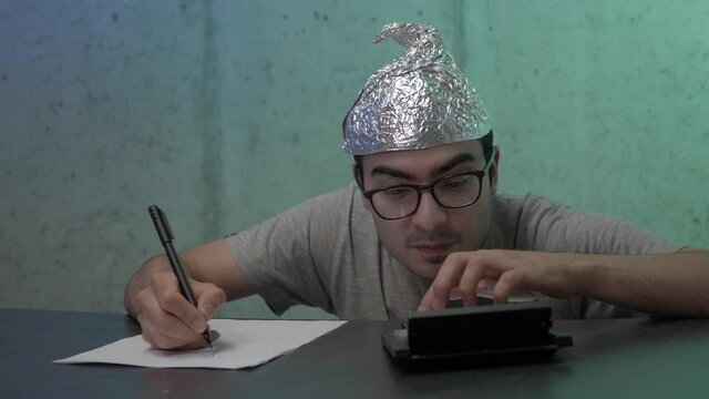 Crazy men going insane calculating and taking notes wearing a tinfoil hat to protect his brain from the 5G waves.