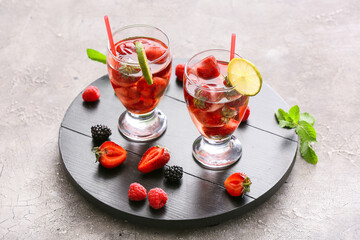 Glasses with ice and frozen berries on grey background