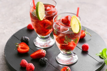 Glasses with ice and frozen berries on grey background