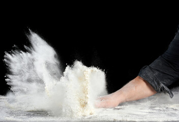 chef in black uniform sprinkles white wheat flour in different directions, product scatters dust