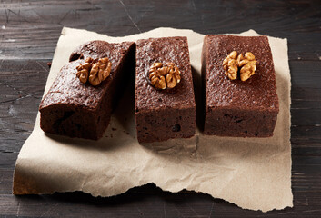 baked pieces of brownie chocolate cake with nuts on a brown piece of paper