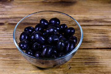 Glass bowl with black olives on wooden table