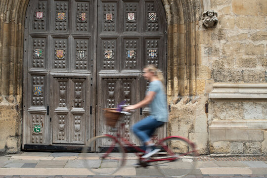 Female Student Riding Old Fashioned Bicycle Around Oxford University College Buildings With Motion Blur