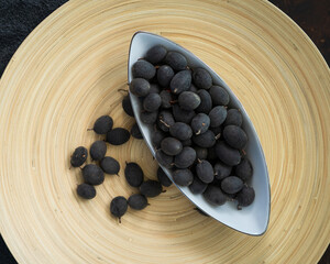 Velvet tamarind fruit ( Dialium cochinchinense) or buah keranji in a wooden bamboo plate background.