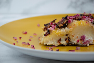 Cod fish with red onion on yellow plate, marble backgound