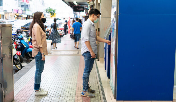 Asian Young People Wearing Face Masks Stand In Line To Using ATM And Self Service Machines.