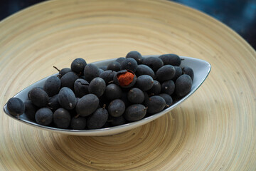 Velvet tamarind fruit ( Dialium cochinchinense) or buah keranji in a wooden bamboo plate background.