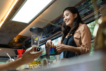 Young Asian woman pouring milk into coffee making late coffee. Professional barista preparing coffee on counter
