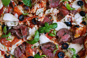 Meat Italian pizza with roast beef, chicken slices, melted cheese, red tomatoes and green basil sauce on a tray decorated by basil leaves and black olives. Pizza time concept. close up