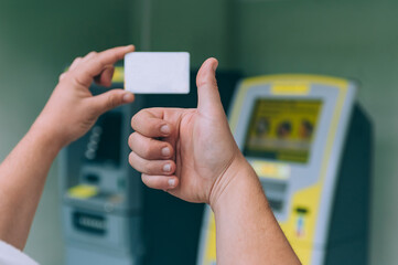 A man holds a credit card in his hands on the background of an ATM.