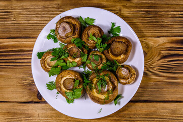 Plate with baked champignons, dill and parsley on a wooden table. Top view