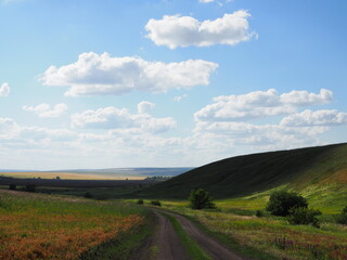 Highway going through rural pastoral landscape. Wheat field with haystacks. Harvesting. Hills and forests. Panorama
