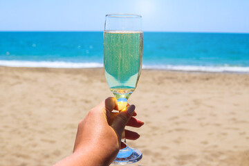 A glass of sparkling wine or champagne in a woman's hand against the backdrop of a seascape. Relax and vacation concept