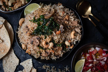 Indian rice and mushroom pilaf along with salad and popadum crackers on dark backround, copy space